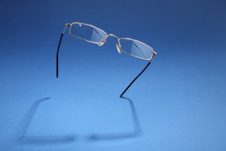 Stylish pair of glasses with metal frame on blue background, space for textの写真素材