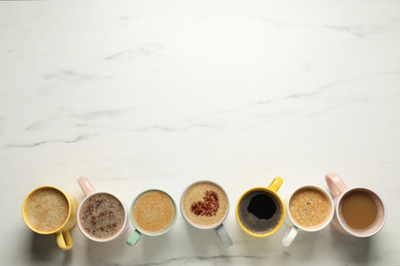 Many cups with different aromatic coffee drinks on white marble table, flat lay. Space for textの写真素材