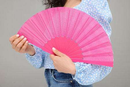 Woman holding hand fan on light gray background, closeupの写真素材