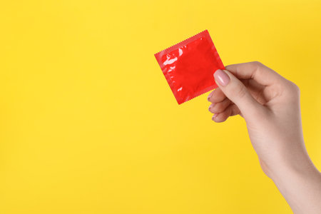 Woman holding condom on yellow background, closeup. Space for textの写真素材