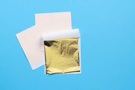 Edible gold leaf sheets on light blue background, top view. Space for textの写真素材