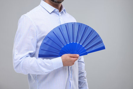 Man holding hand fan on light gray background, closeupの写真素材