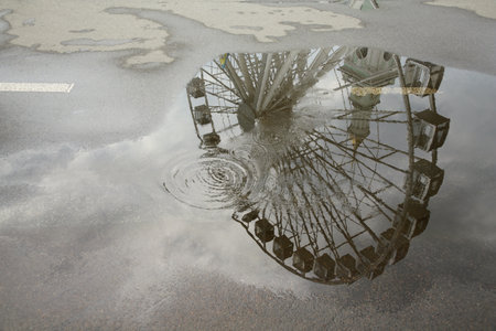 Reflection of Ferris wheel in puddle on asphalt outdoorsの写真素材