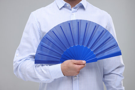 Man holding hand fan on light gray background, closeupの写真素材