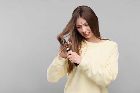 Upset woman brushing her hair on grey background, space for text. Alopecia problemの写真素材