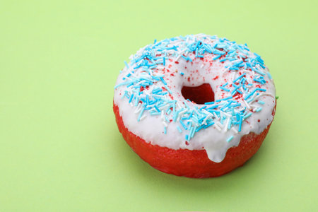 Glazed donut decorated with sprinkles on green background, closeup. Space for text. Tasty confectioneryの写真素材