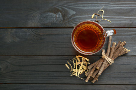 Aromatic licorice tea in cup and dried sticks of licorice root on black wooden table, flat lay. Space for textの写真素材