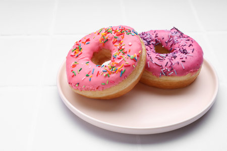 Glazed donuts decorated with sprinkles on white tiled table, closeup. Space for text. Tasty confectioneryの写真素材