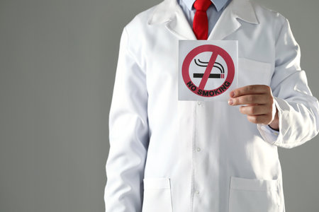 Doctor holding card with no smoking sign on gray background, closeup. Space for textの写真素材
