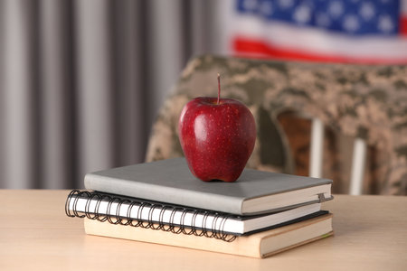 Notebooks and apple on wooden table near flag of United States indoors. Military educationの写真素材