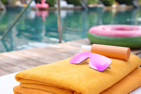 Beach towels, sunglasses and sunscreen on sun lounger near outdoor swimming pool, closeup. Luxury resortの写真素材