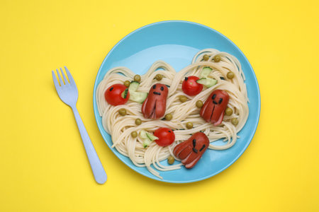 Creative serving for kids. Plate with cute octopuses made of sausages, pasta and vegetables on yellow table, flat layの写真素材