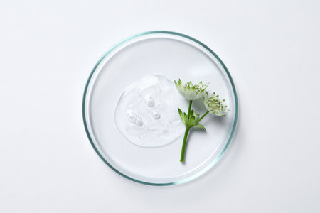 Petri dish with sample of cosmetic oil and flowers on white background, top viewの写真素材