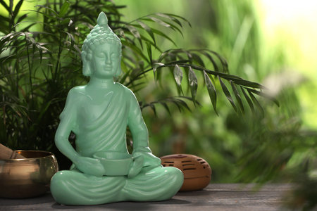 Buddhism religion. Decorative Buddha statue and singing bowl on wooden table outdoors, space for textの写真素材