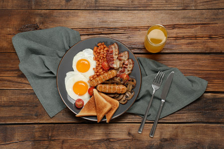 Plate with fried eggs, sausages, mushrooms, beans, bacon and toasted bread on wooden table, flat lay. Traditional English breakfastの写真素材