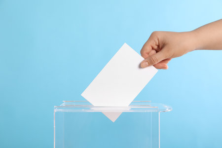 Woman putting her vote into ballot box on light blue background, closeupの写真素材