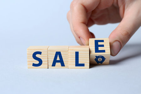 Woman making word Sale with wooden cubes on light blue background, closeupの写真素材