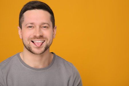 Happy man showing his tongue on orange background. Space for textの写真素材