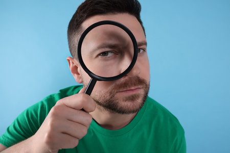 Man looking through magnifier glass on light blue backgroundの写真素材