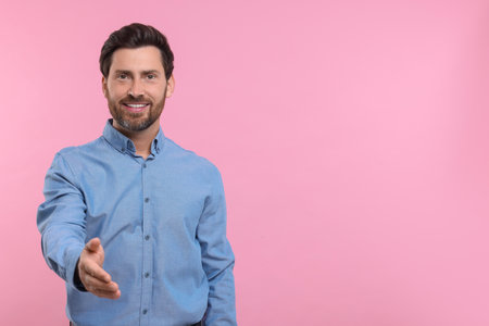 Happy man welcoming and offering handshake on pink background. Space for textの写真素材