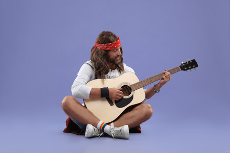 Stylish hippie man playing guitar on violet backgroundの写真素材