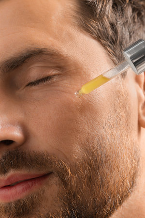 Handsome man applying cosmetic serum onto his face, closeupの写真素材