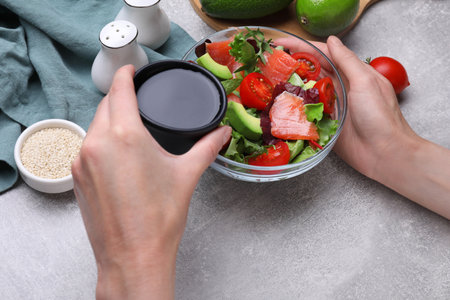 Woman adding soy sauce to tasty salad at gray table, closeupの写真素材