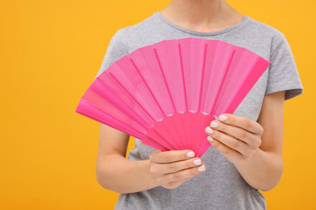 Woman holding hand fan on orange background, closeupの写真素材