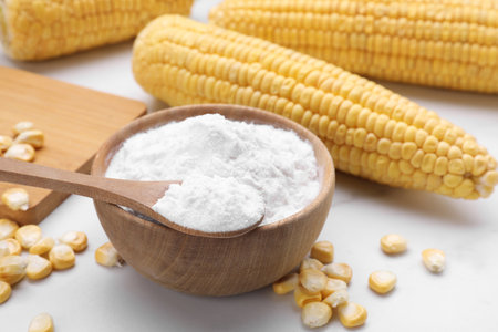 Bowl with corn starch, ripe cobs and kernels on white tableの写真素材