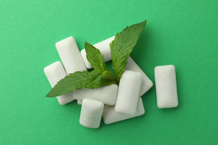 Tasty white chewing gums and mint leaves on green background, top view