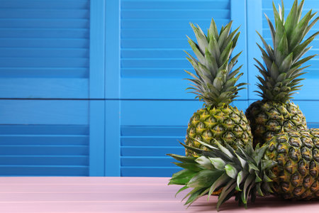 Delicious ripe pineapples on pink table near blue wall. Space for textの写真素材
