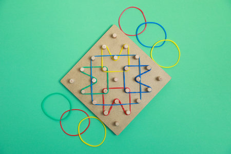 Wooden geoboard with rubber bands on green background, flat lay. Educational toy for motor skills developmentの写真素材