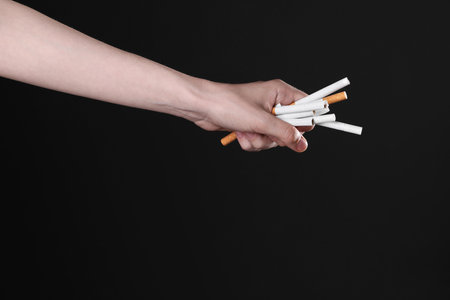 Stop smoking concept. Woman holding cigarettes on black background, closeupの写真素材