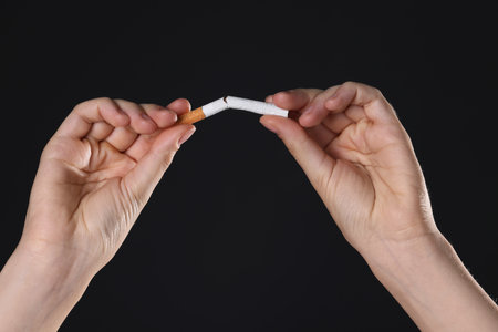Stop smoking concept. Woman breaking cigarette on black background, closeupの写真素材
