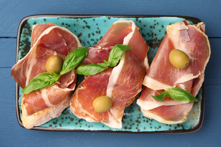 Tasty sandwiches with cured ham and basil leaves on blue wooden table, top viewの写真素材
