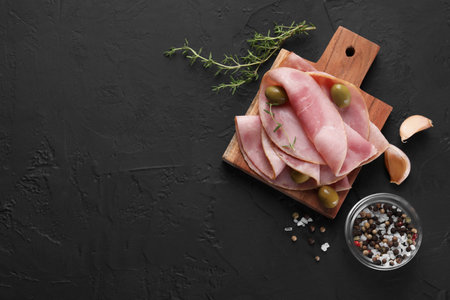Tasty ham with olives, garlic, thyme and spices on black textured table, flat lay. Space for textの写真素材