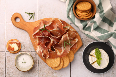 Slices of tasty cured ham, rosemary and crackers on tiled table, flat layの写真素材