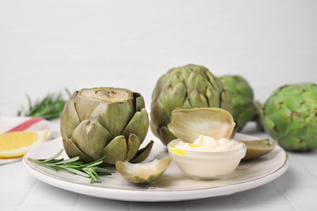 Delicious cooked artichokes with tasty sauce served on white table, closeupの写真素材
