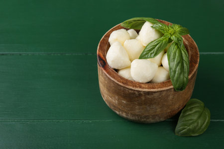 Tasty mozzarella balls and basil leaves in bowl on green wooden table. Space for textの写真素材