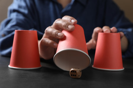 Woman playing thimblerig game with red cups and dice at black table, closeupの写真素材