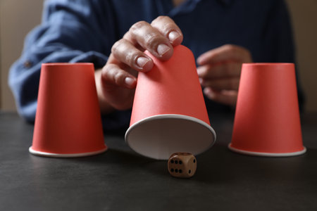 Woman playing thimblerig game with red cups and dice at black table, closeupの写真素材