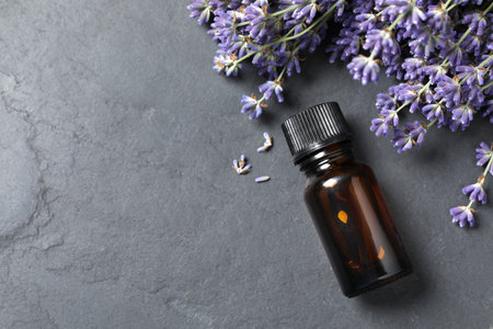 Bottle with essential oil near lavender on gray textured table, flat lay. Space for textの写真素材