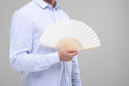 Man holding hand fan on light gray background, closeupの写真素材