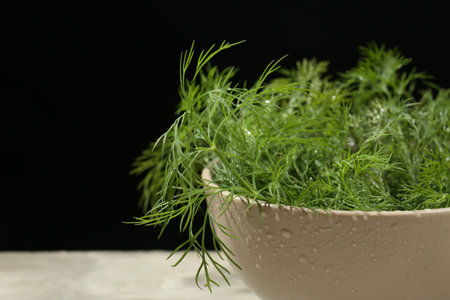 Bowl of fresh green dill with water drops on light gray table against black background, closeup. Space for textの写真素材