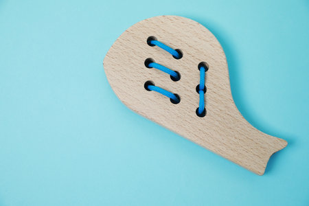 Wooden whale figure with holes and lace on light blue background, top view and space for text. Educational toy for motor skills developmentの写真素材