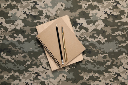 Notebooks, pen and pencil on camouflage background, top view. Military educationの写真素材