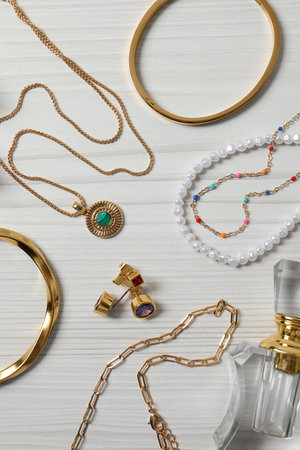 Flat lay composition of beautiful bijouterie and perfume bottle on white wooden table