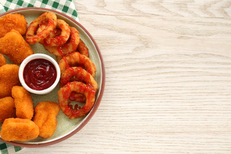 Tasty fried onion rings, chicken nuggets and ketchup on white wooden table, top view. Space for textの写真素材