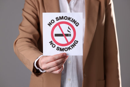 Woman holding card with no smoking sign on gray background, closeupの写真素材