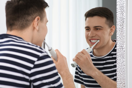 Man brushing his teeth with electric toothbrush near mirror in bathroomの写真素材